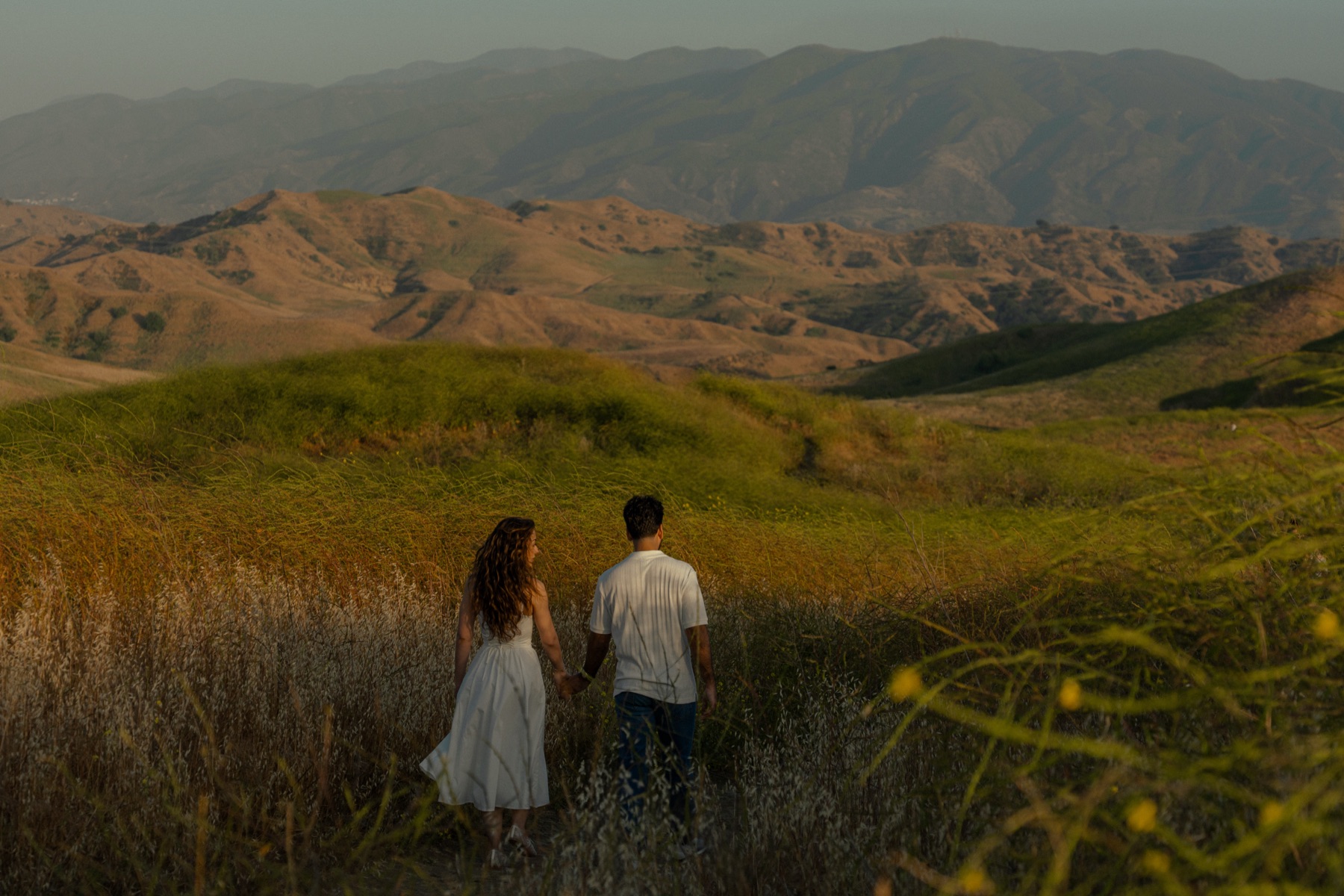 Lily and Nima holding hands, walking through golden sunset hills